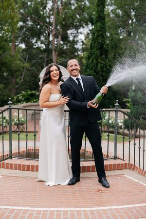 A joyful celebration with champagne being sprayed on a brick patio during a wedding ceremony.