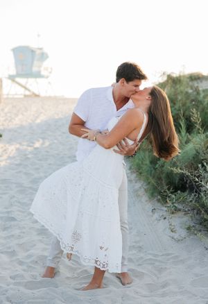 A romantic beach moment with a lifeguard tower visible in the background.