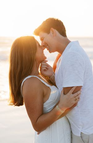 A romantic couple embraces during sunset at the beach, sharing an intimate moment in warm golden light.