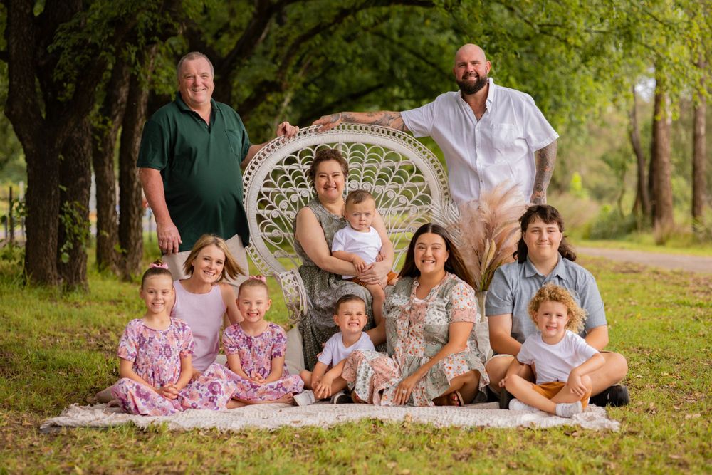 Large family group portrait outdoors with peacock chair and pampas grass decor.