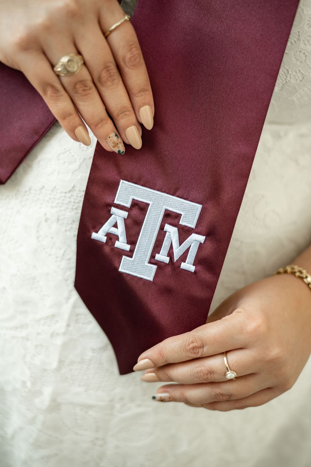 Hands with manicured nails hold a maroon fabric with white "M" lettering being applied or peeled off.
