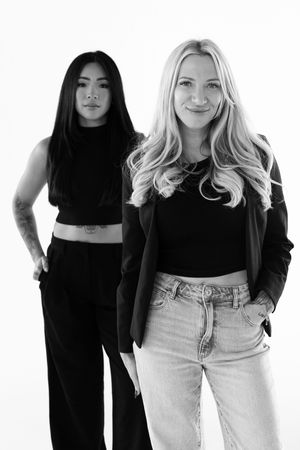 Black and white fashion portrait of women in contrasting dark and light outfits standing against white background.