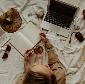 Flatlay workspace scene with laptop, straw hat, and scattered papers on white bedding.