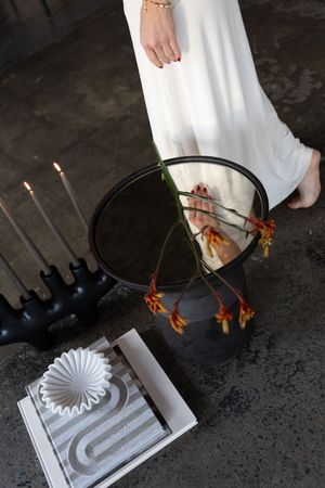 White fabric and orange flowers beside candles and decorative geometric pattern on dark background with mirror reflection.