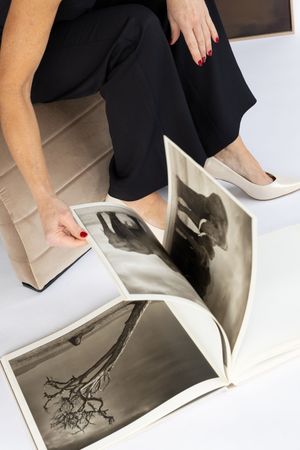 Person in black pants and white heels sits with an open art book displaying black and white photographs.