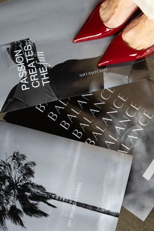 Red patent leather stiletto heels rest on black and white fashion magazines with palm tree photography.