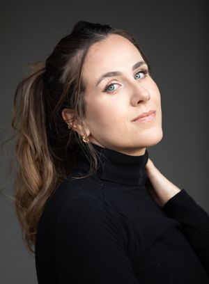 Portrait of someone in a black turtleneck against dark background with soft lighting.