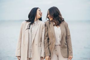 A couple in neutral-toned outfits walks together along a misty beach shoreline at sunset.
