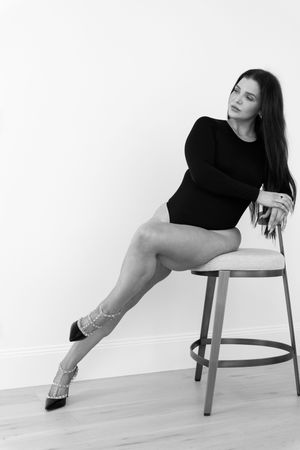 Black and white portrait of a dancer in a black leotard striking an elegant pose on a bar stool.