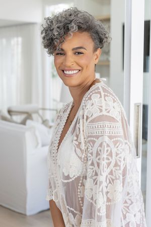 A person wearing a white lace dress smiles brightly in a light-filled interior space.