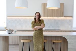 Woman in olive green dress leans against modern kitchen counter with pendant lights overhead.