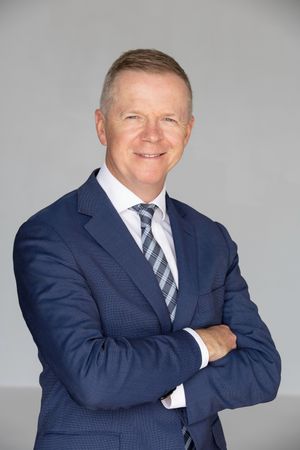 Professional headshots of a person in a navy suit and striped tie against a gray background.