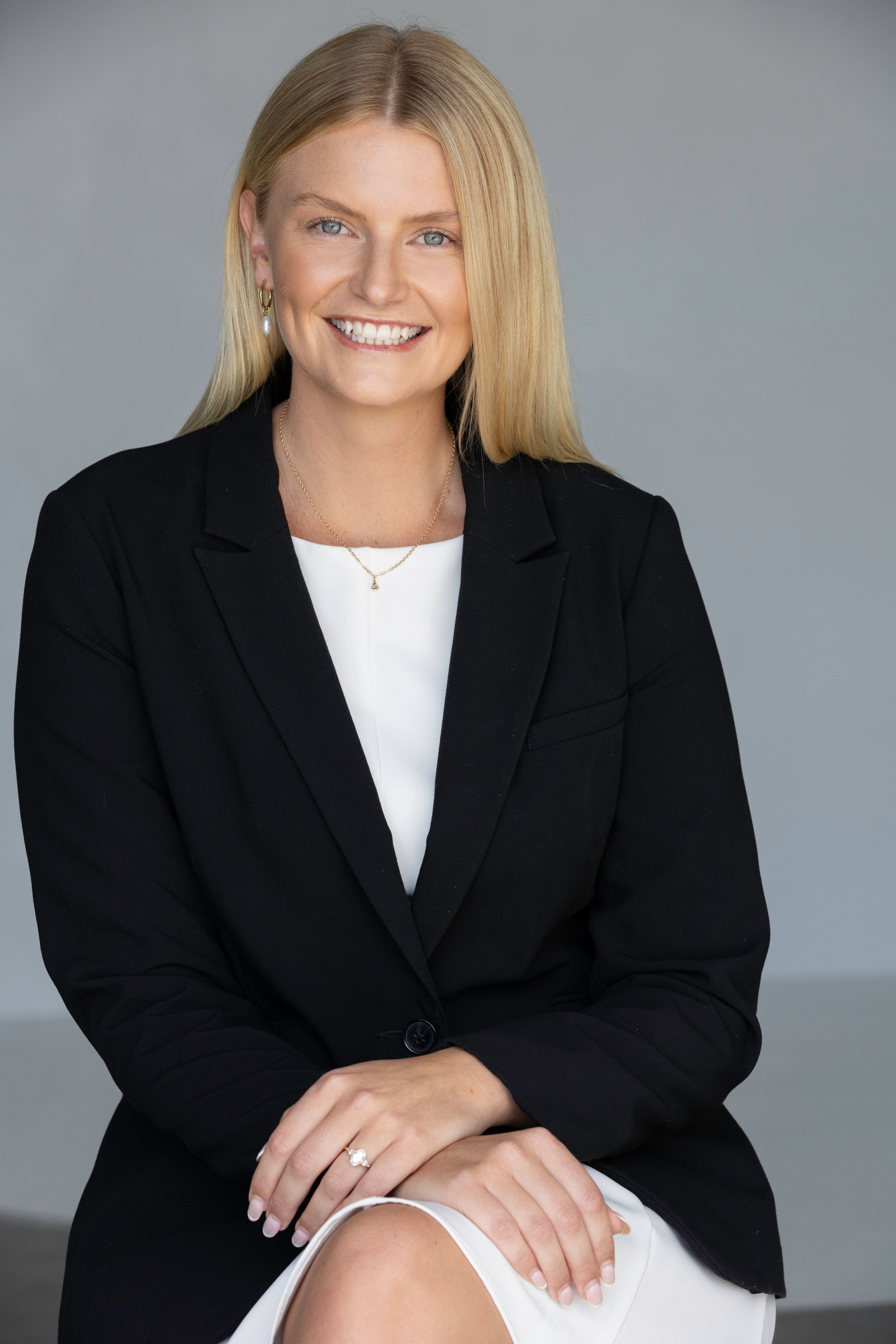 Professional headshots of a person in a black blazer and white top against a gray backdrop.