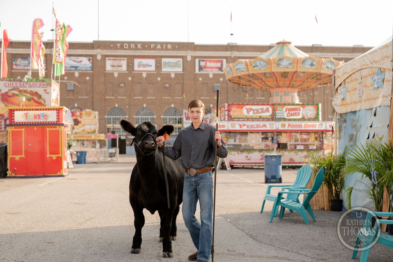 A black show cow walks with handler past carnival vendor booths at state fair.