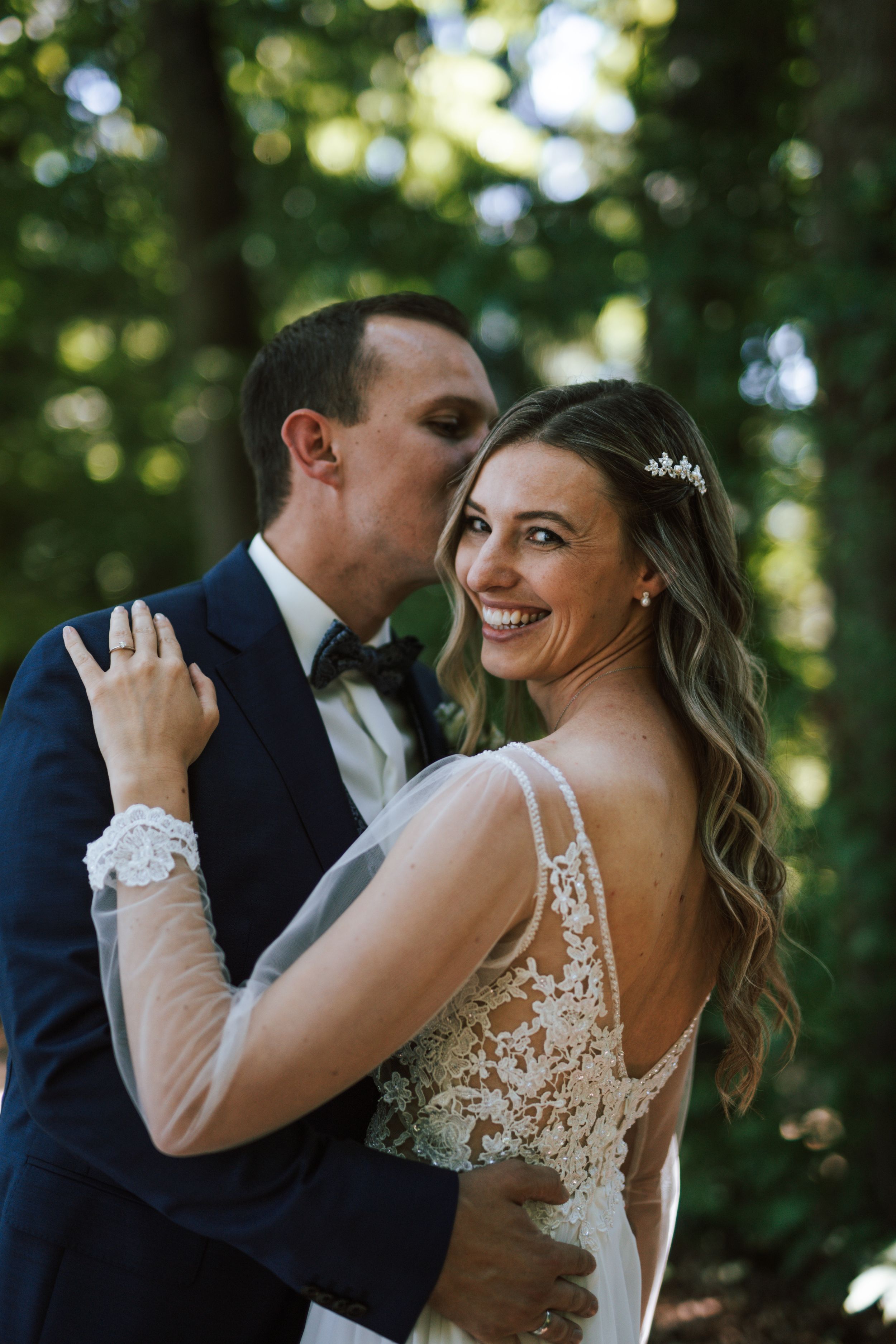 A romantic wedding moment captured in a forest setting with natural lighting.