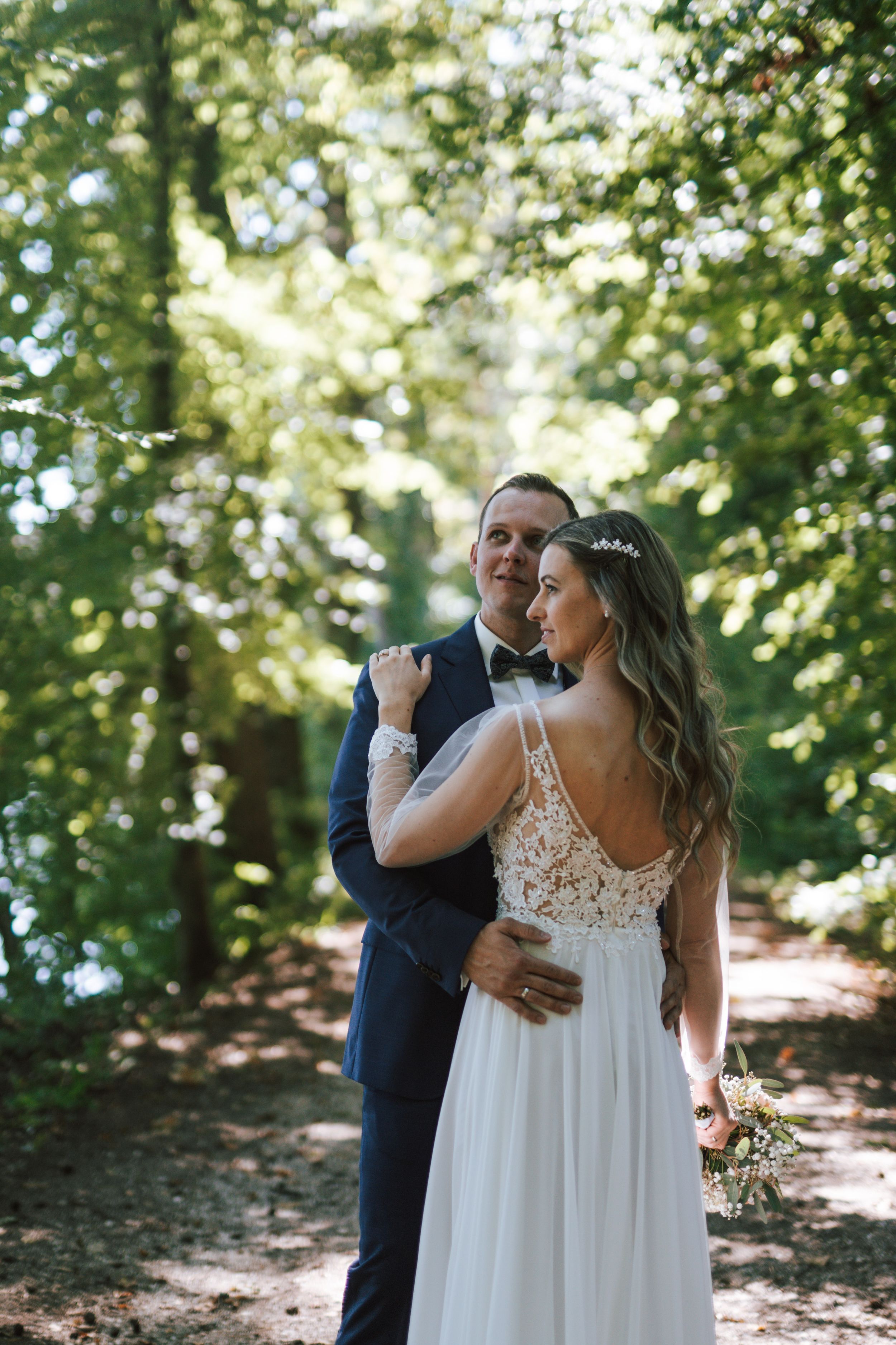 A tender wedding embrace photographed in a sun-dappled woodland setting.