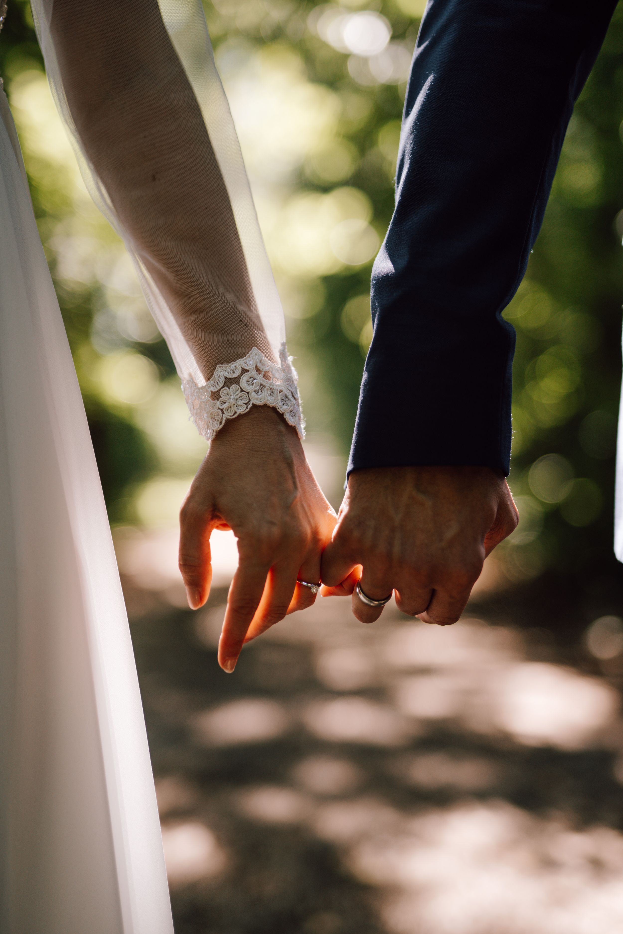 Close-up of newlyweds' hands with wedding rings and lace detail.