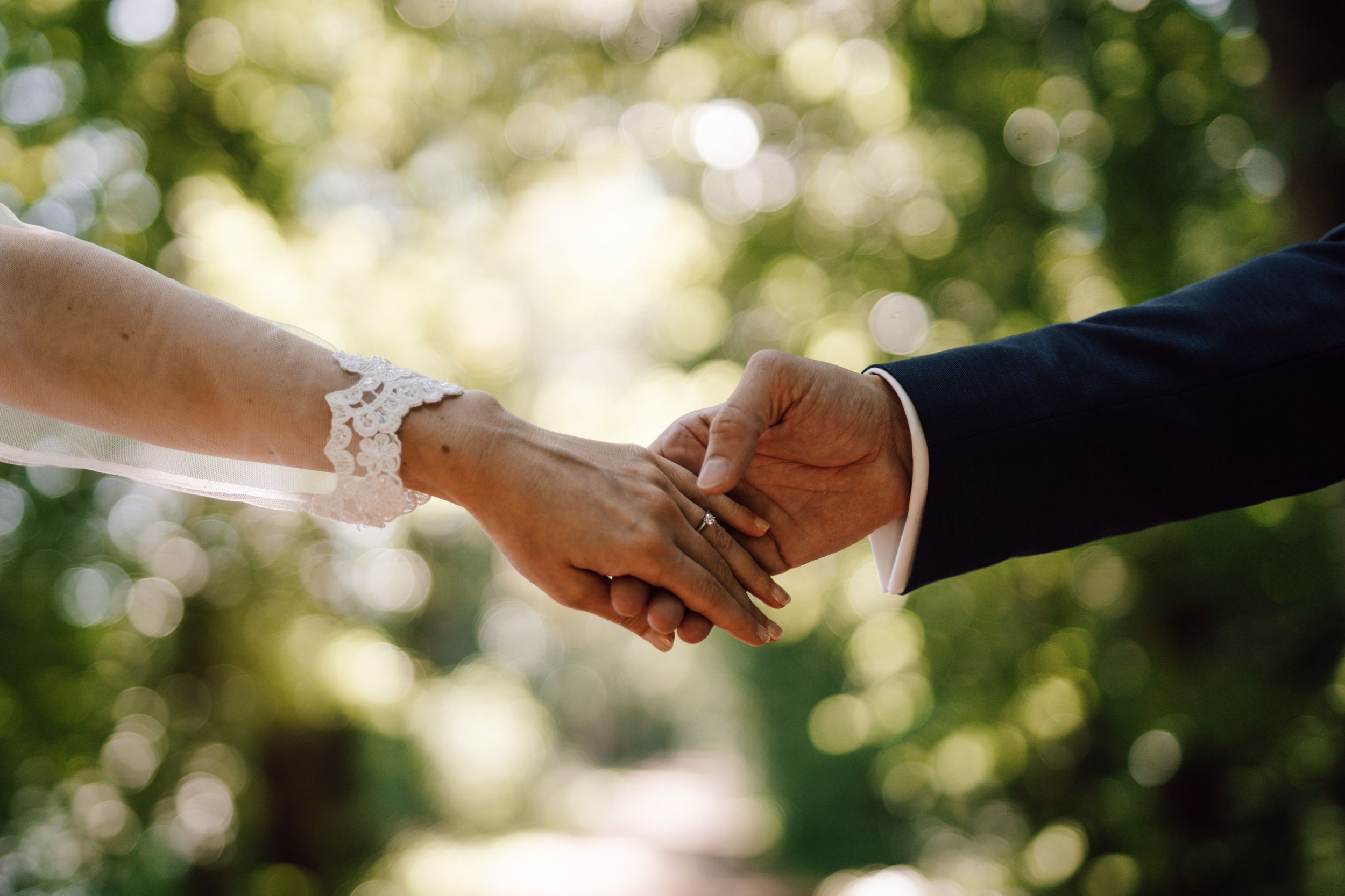 Intimate hand-holding moment between newlyweds with delicate lace details.
