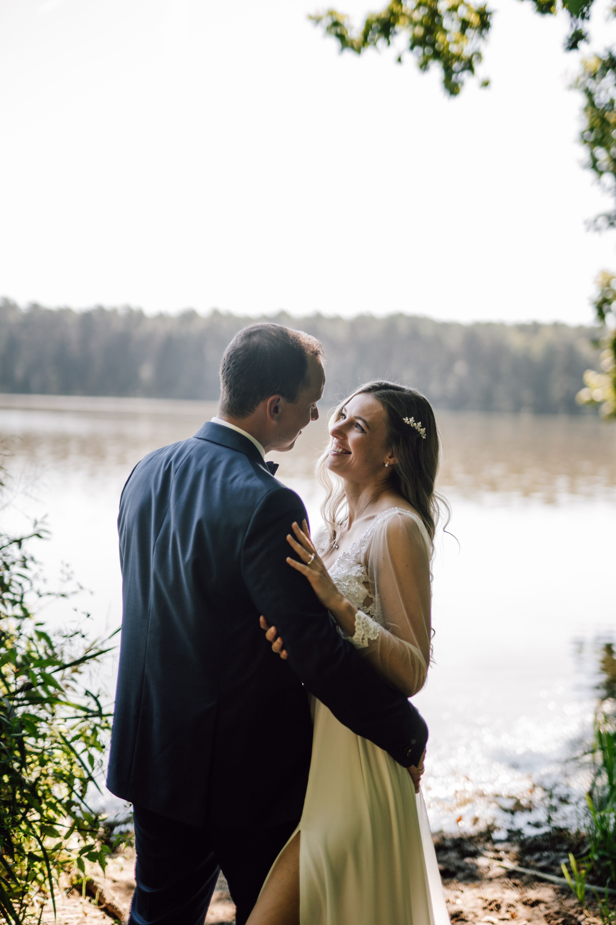 A joyful wedding moment captured by a serene lake with forest backdrop.