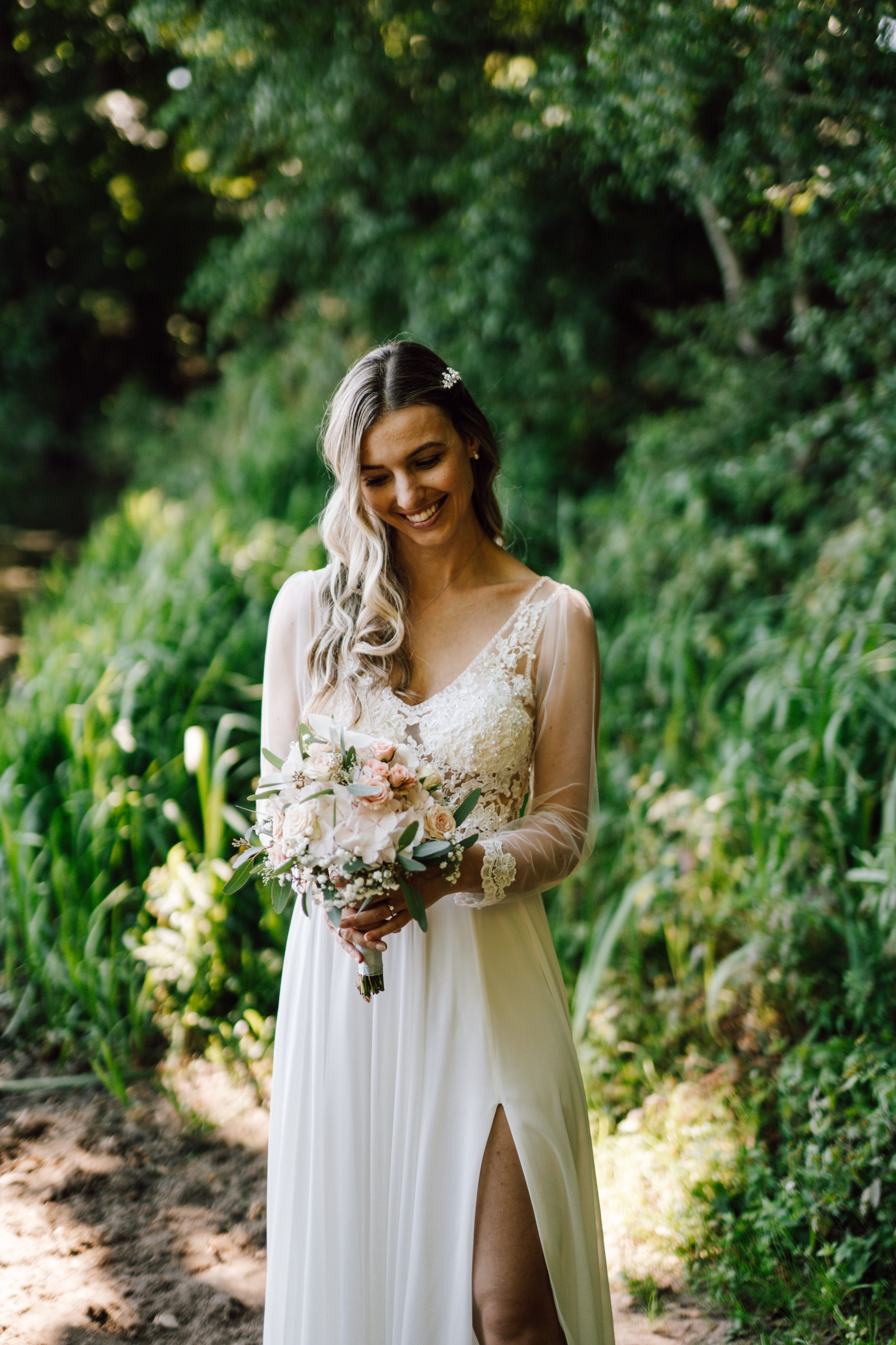A beautiful bride in a flowing white dress holds a delicate bouquet in a garden setting.