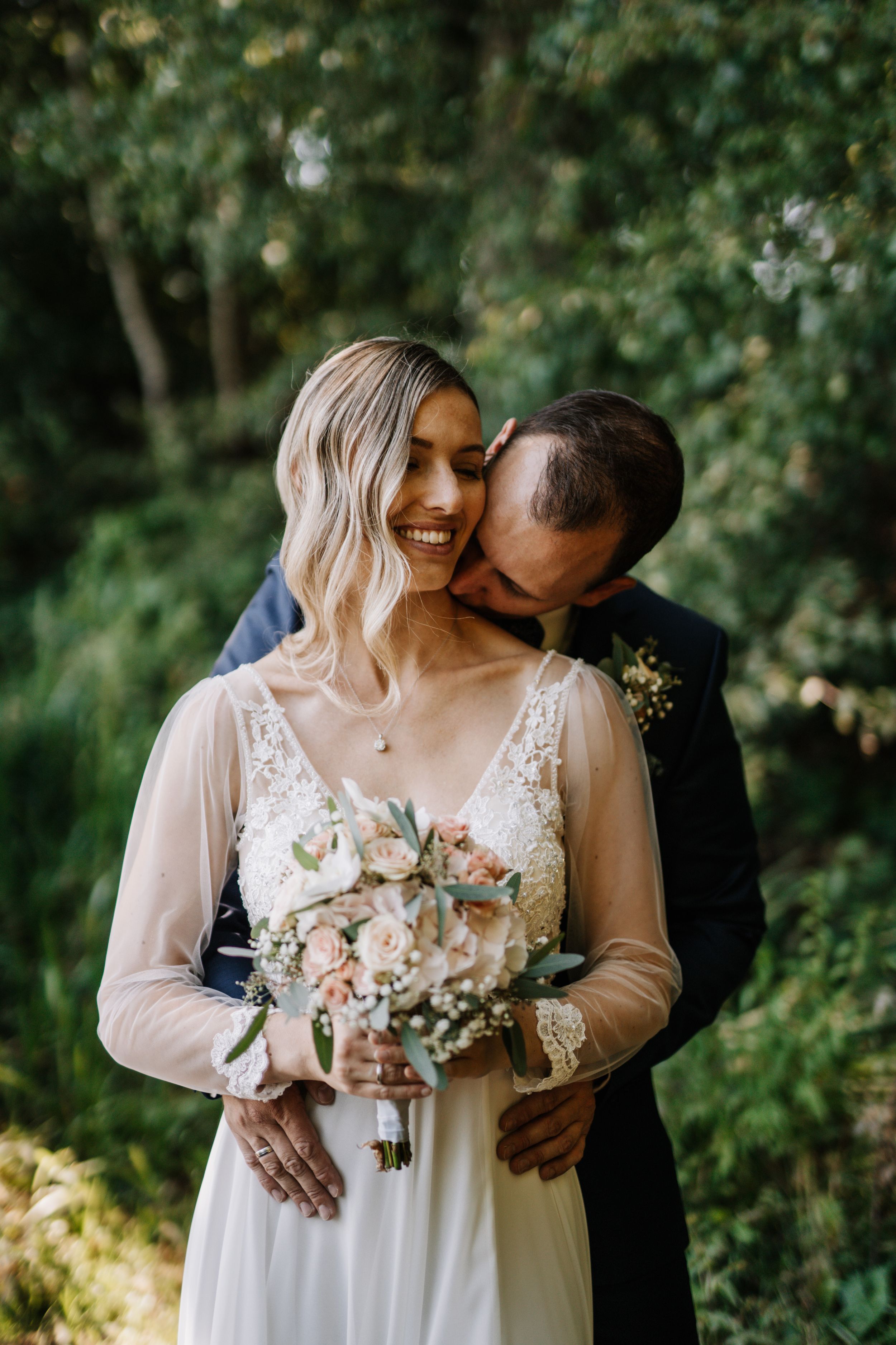 Romantic wedding couple embracing in a sunlit garden setting.
