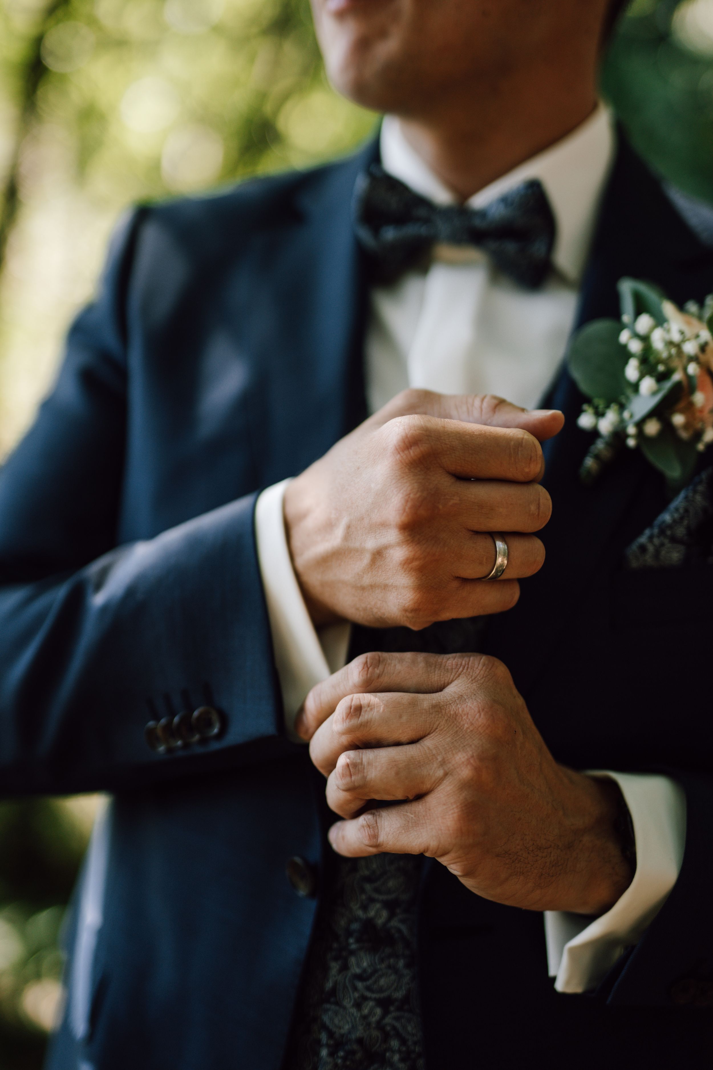 Close-up details of groom's hands adjusting suit and boutonniere.