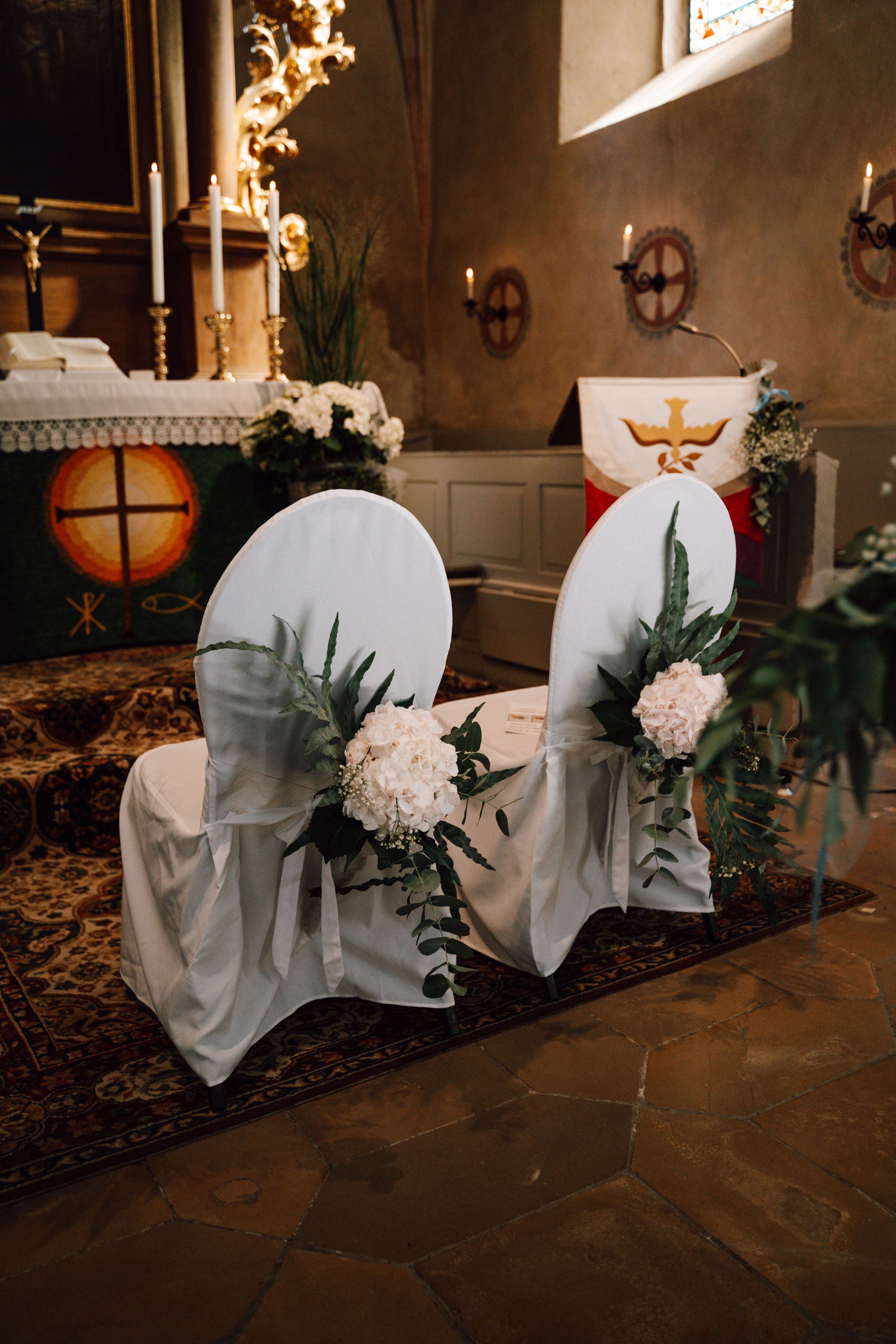 Church pews decorated with white covers and floral arrangements for a wedding ceremony.