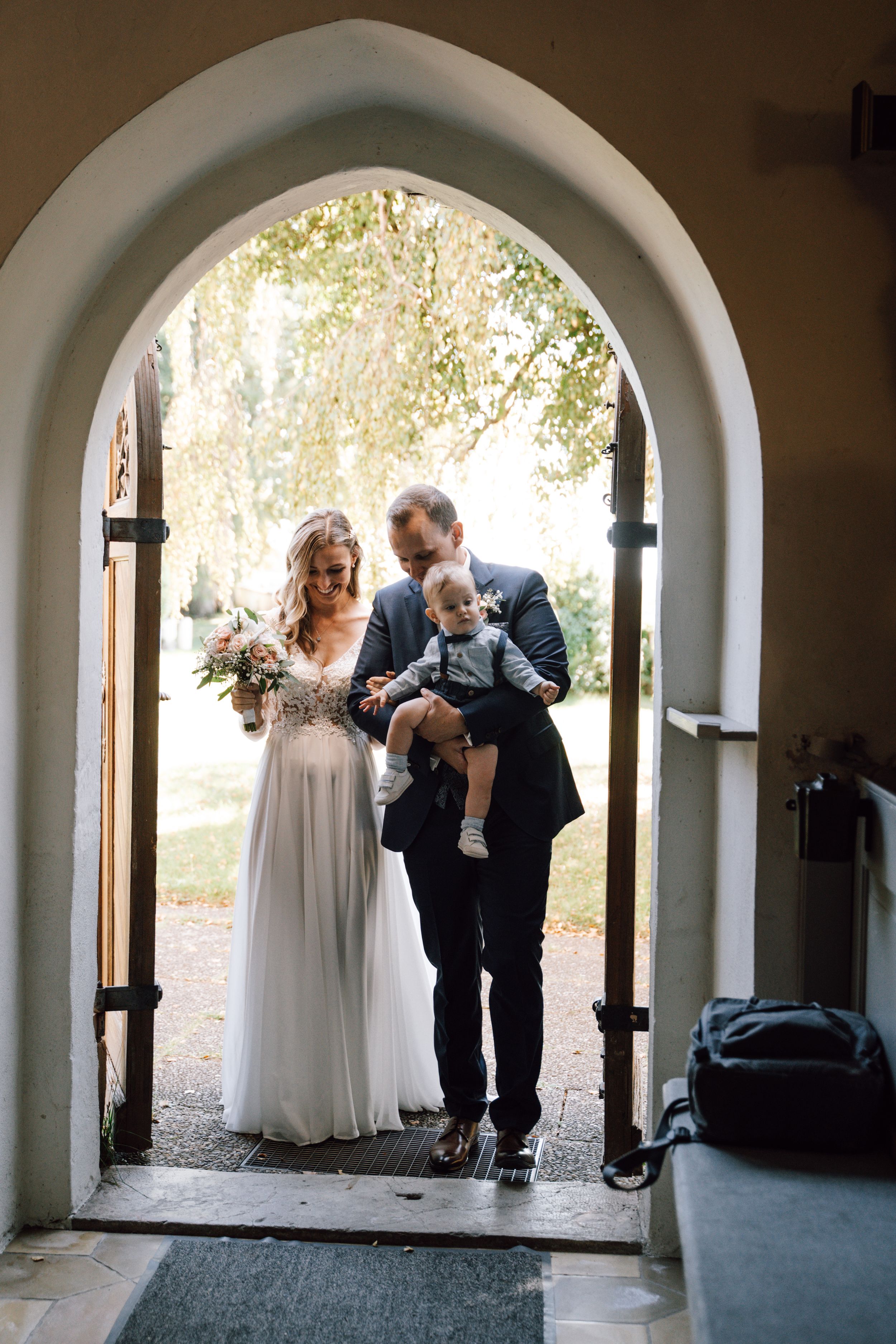 Wedding couple poses beneath arched stone walkway in romantic outdoor setting.