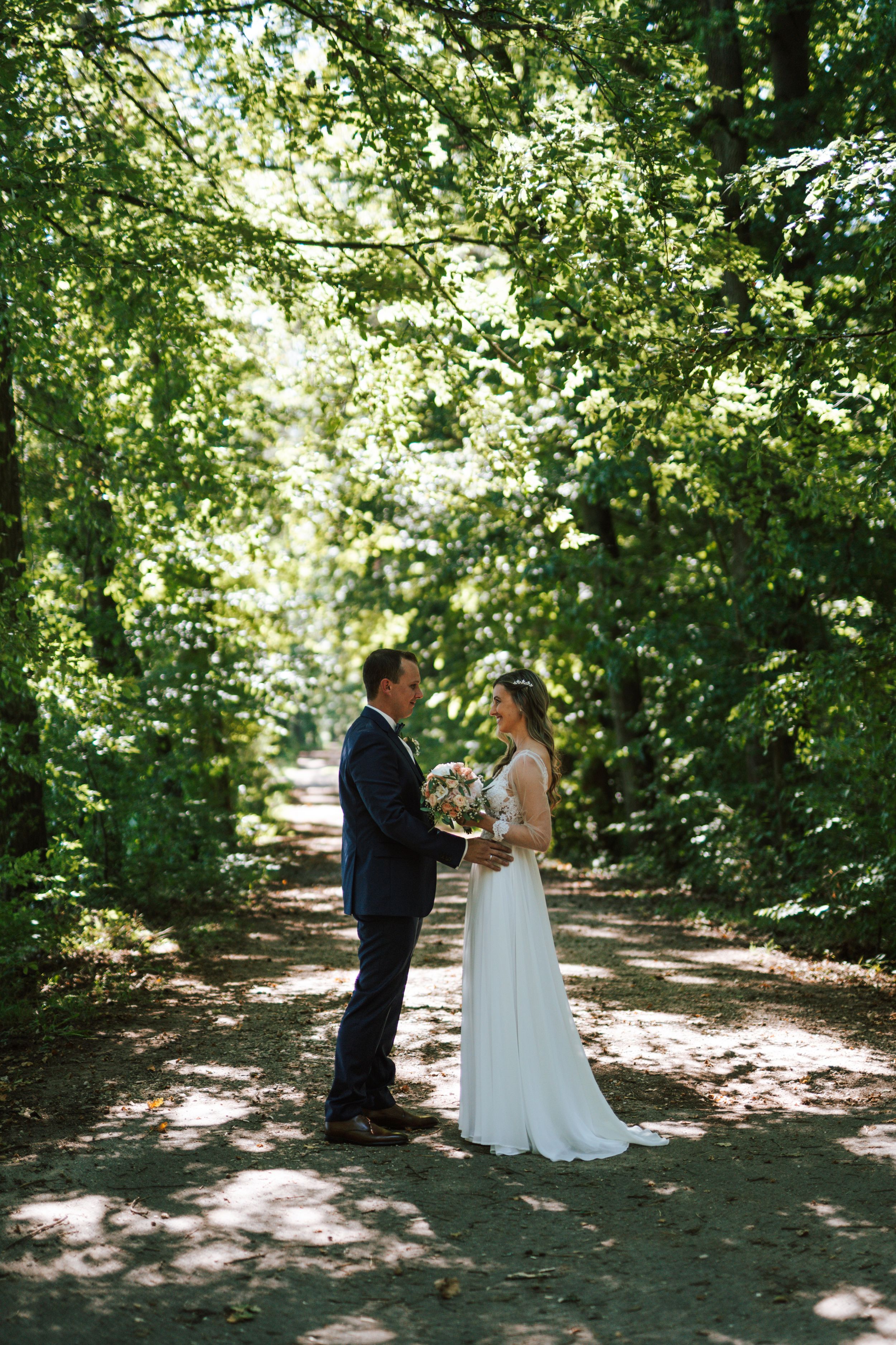 Couple sharing their first look in a sunlit wooded area during their wedding day.