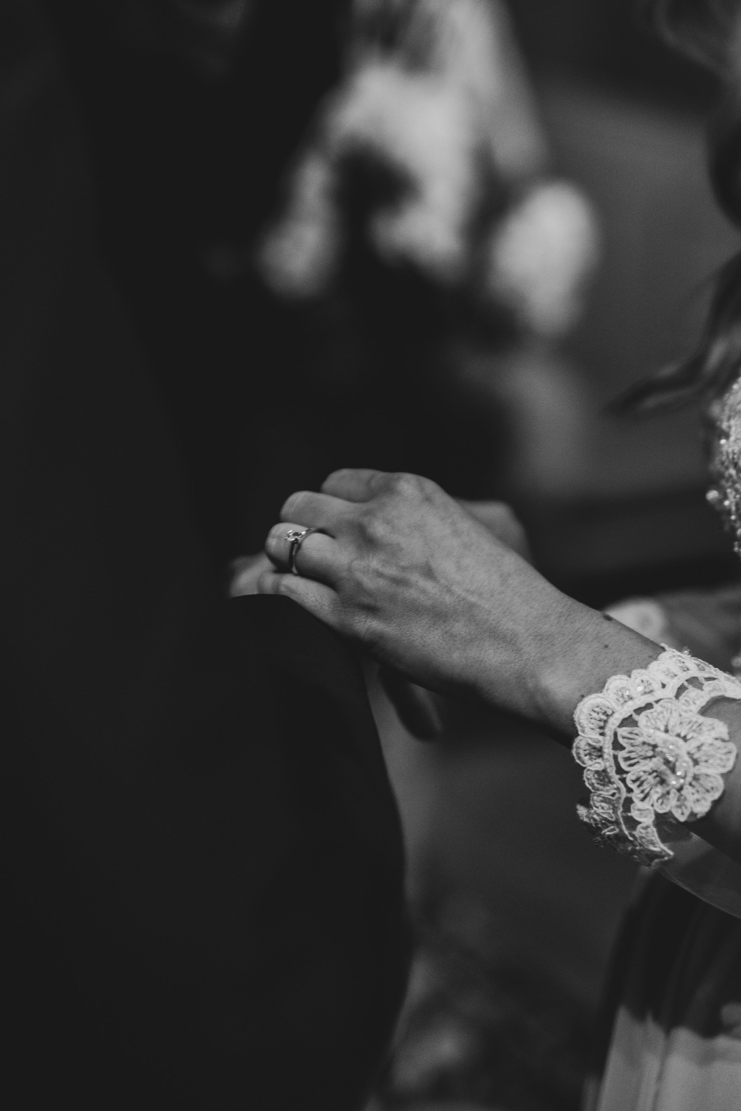Black and white close-up of hands with lace detail during wedding ceremony.