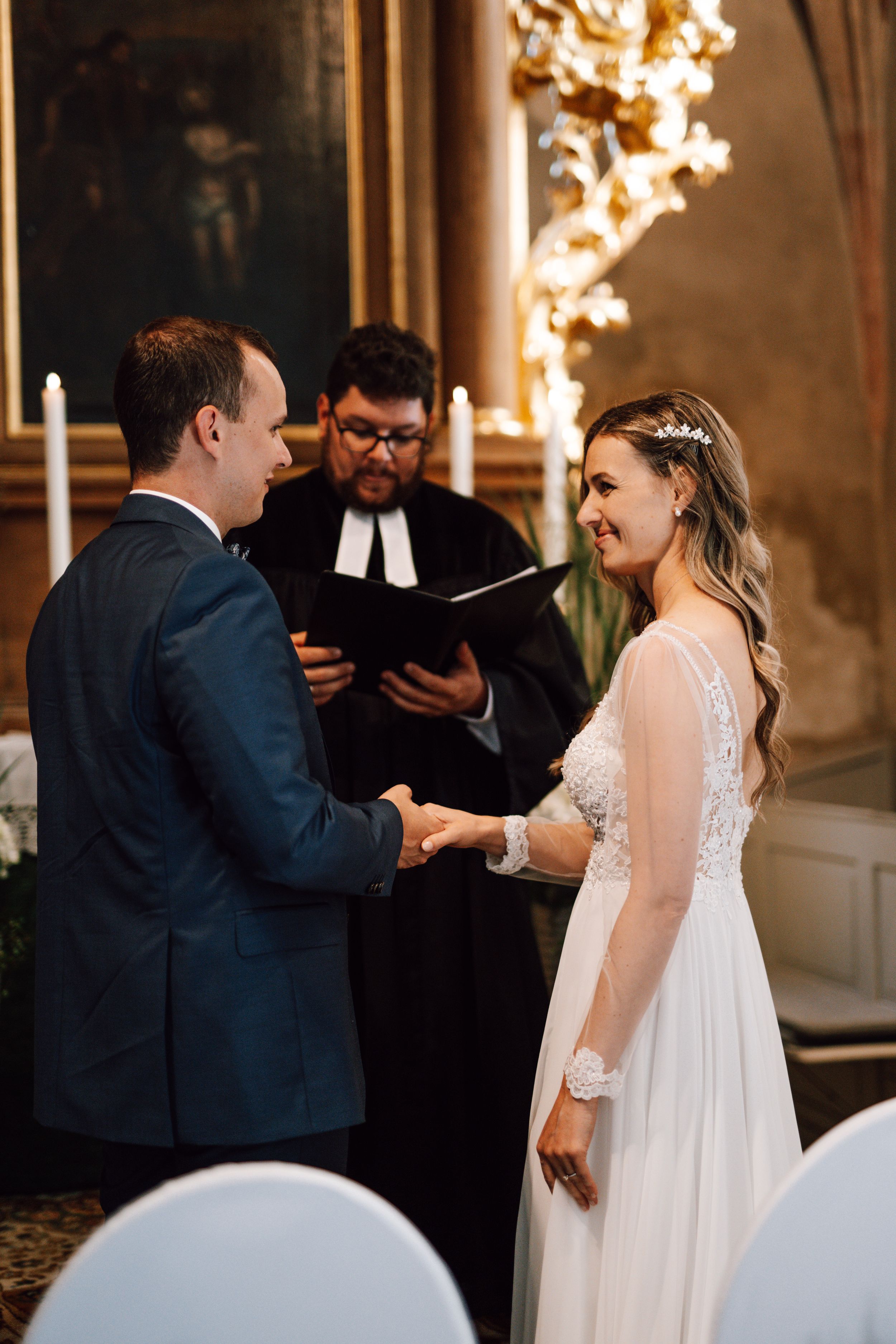 Wedding ceremony taking place in an ornate venue with gold decor and elegant lighting.