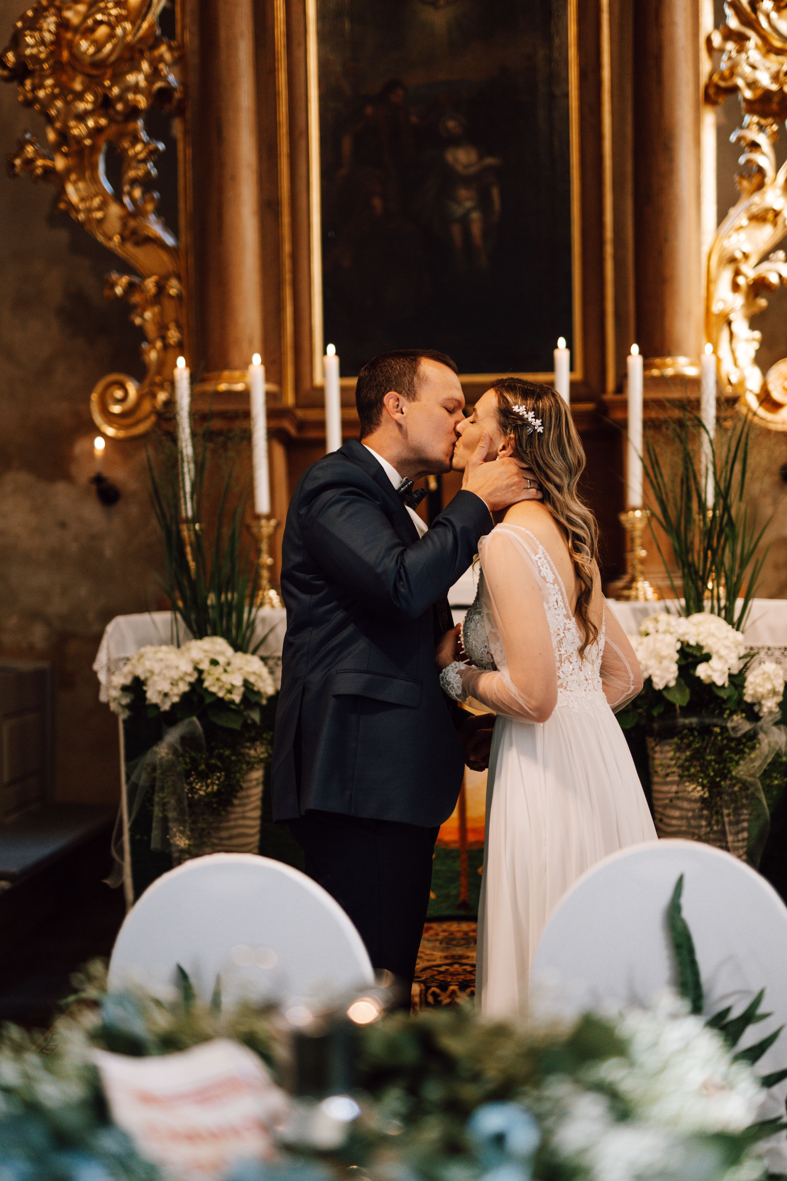First kiss moment at a wedding ceremony with floral decorations in the foreground.