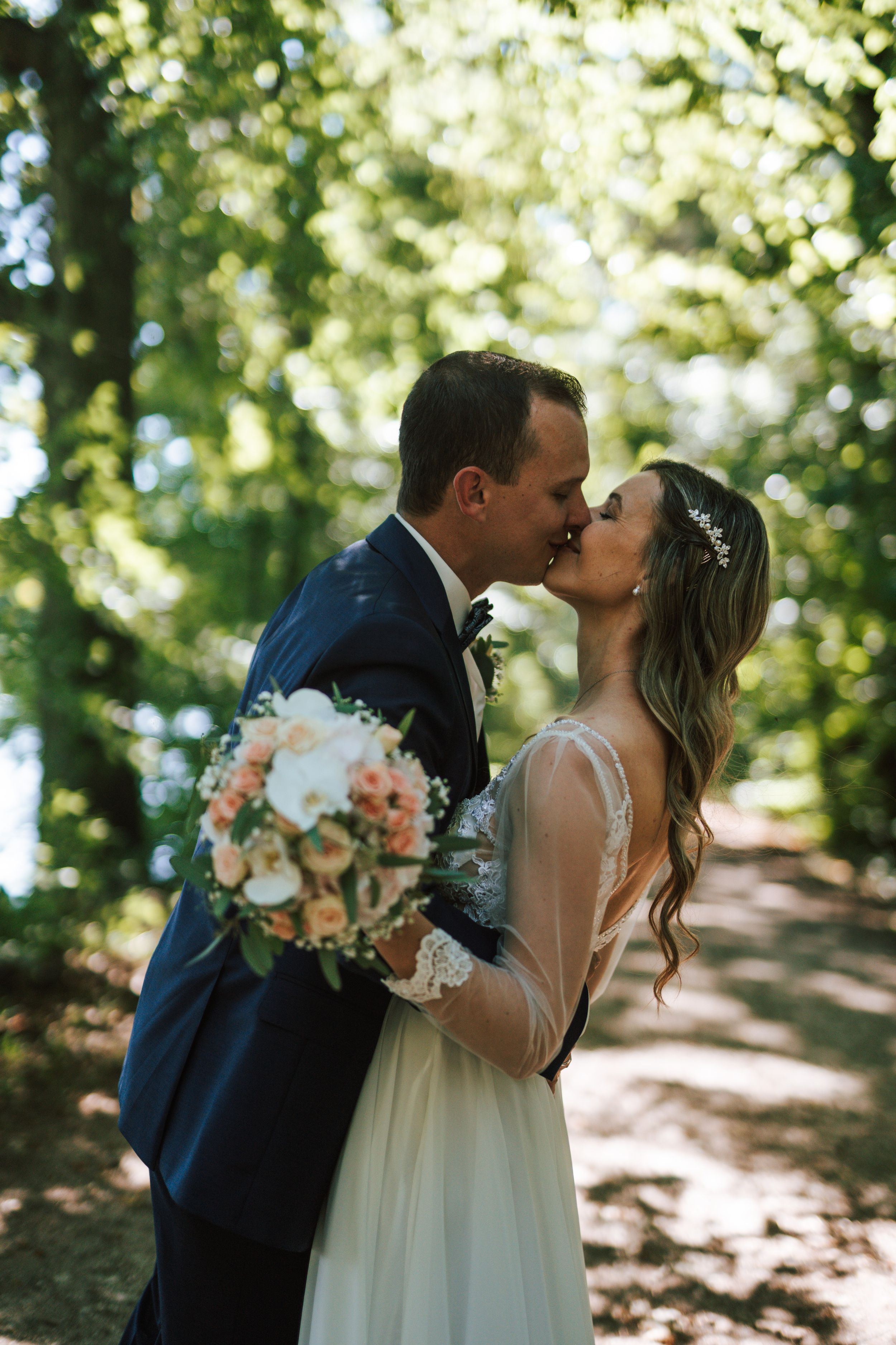 Newlyweds share intimate moments in a sun-dappled forest setting with romantic lighting.