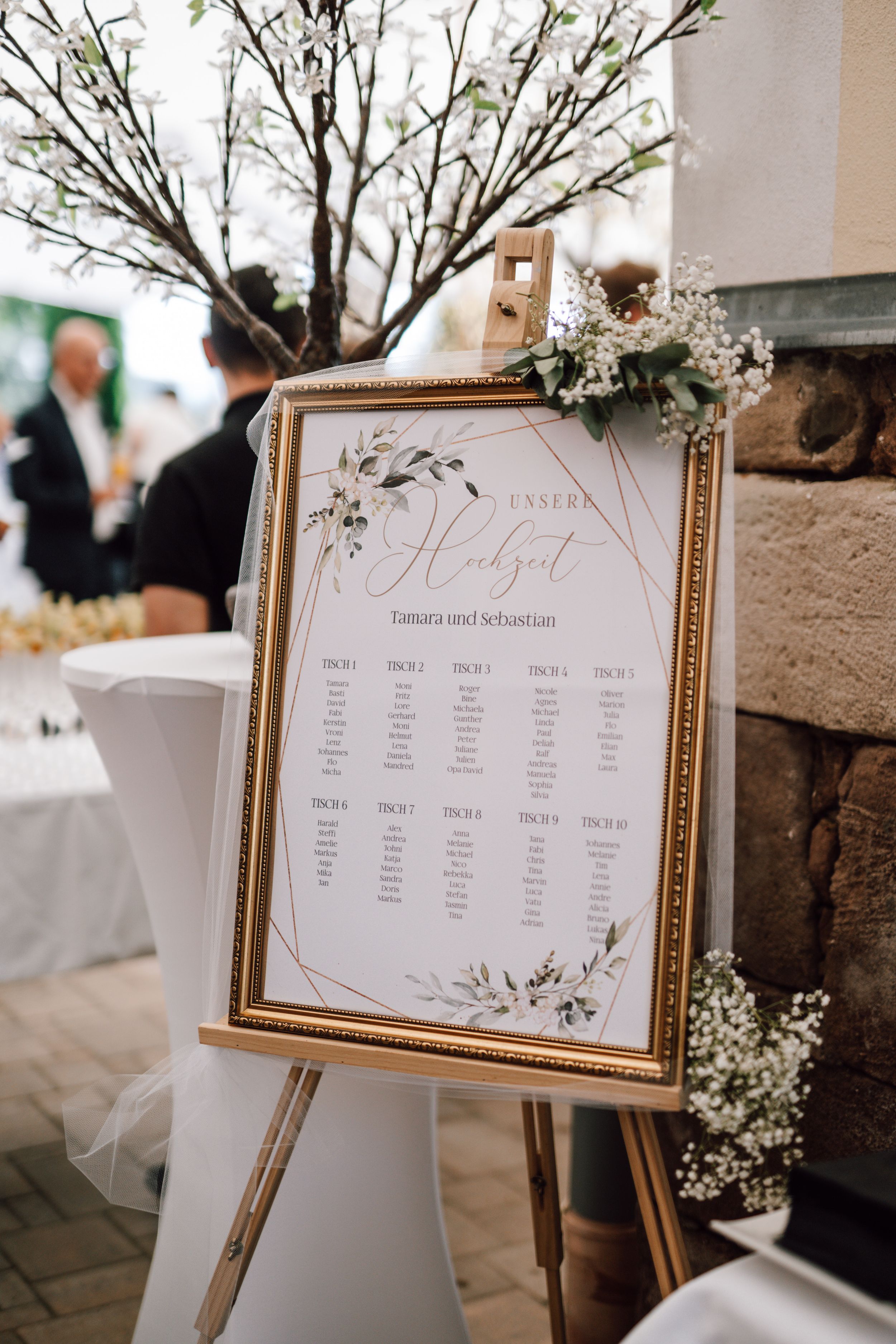 Elegant wedding seating chart displayed in gold frames with floral decorations.