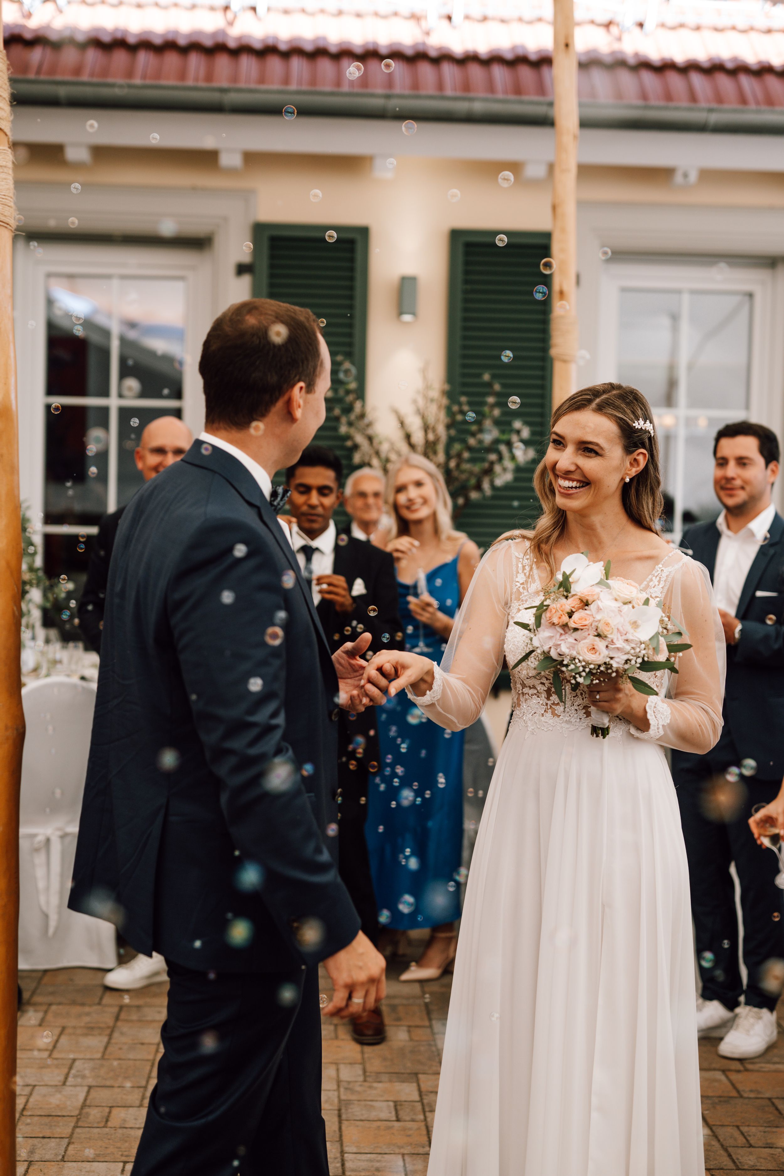 Wedding celebration under a white tent with guests mingling and dancing on a stone patio.