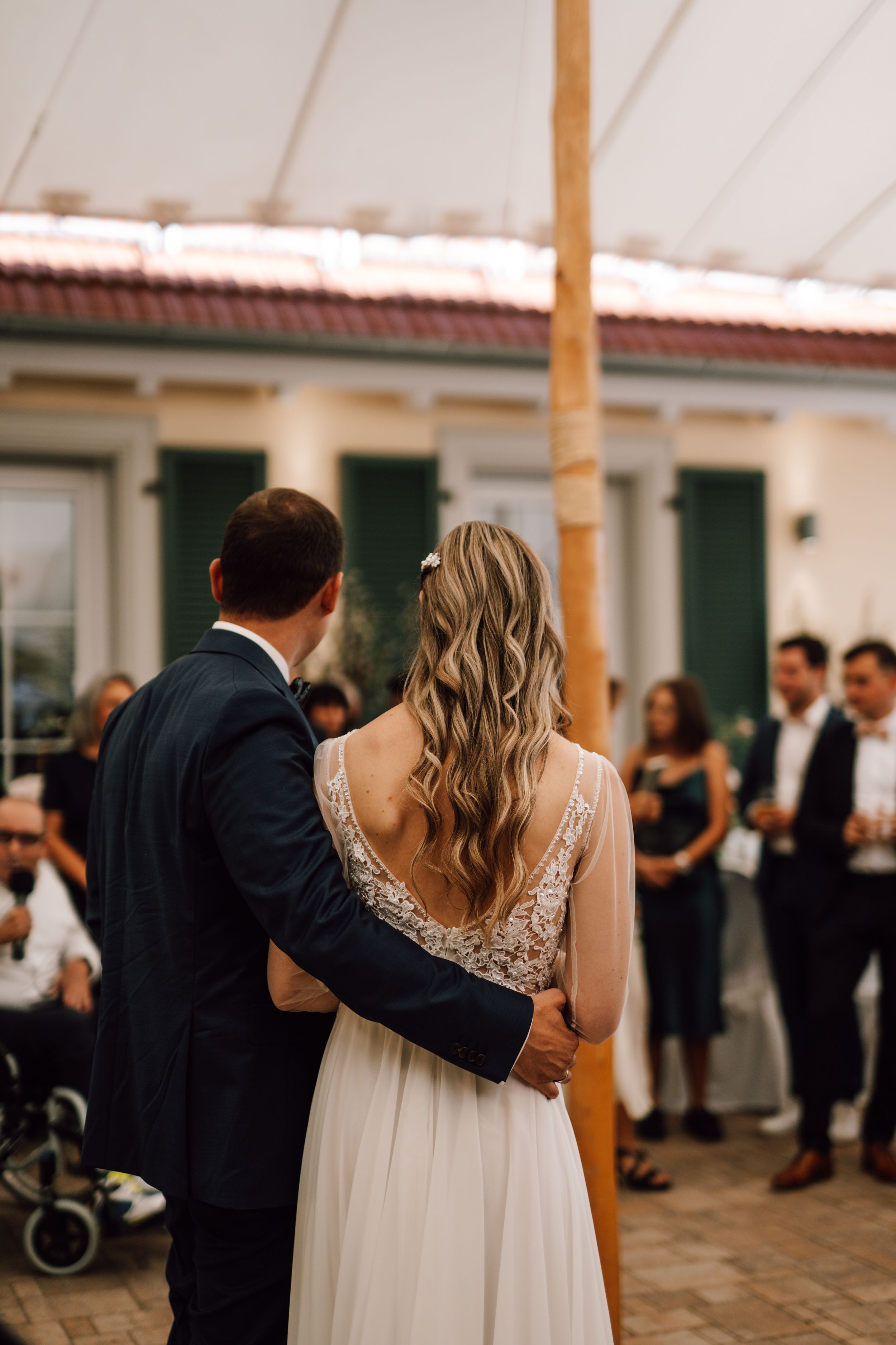Couple dancing together at an outdoor wedding reception under a white tent canopy.