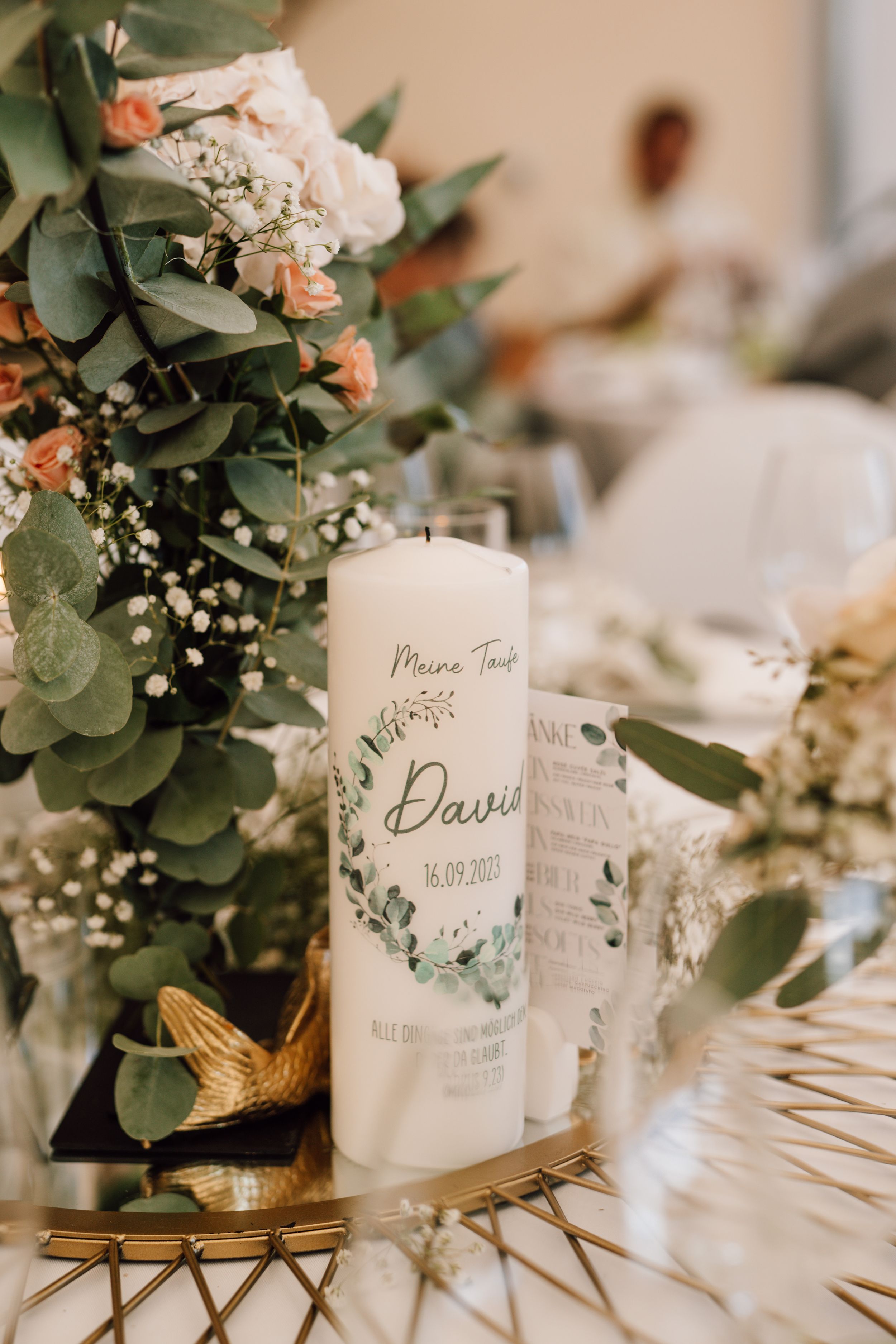 Wedding table decorations featuring personalized candles and eucalyptus greenery on gold accents.