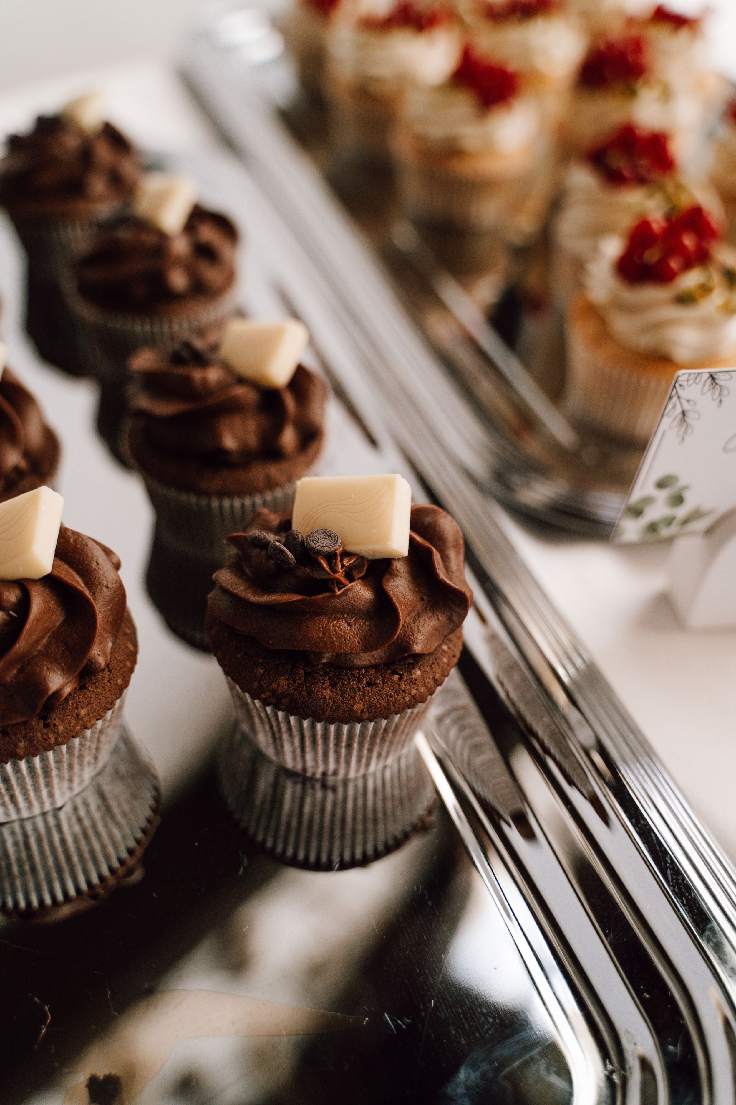 Chocolate cupcakes with dark frosting arranged on a silver serving tray.