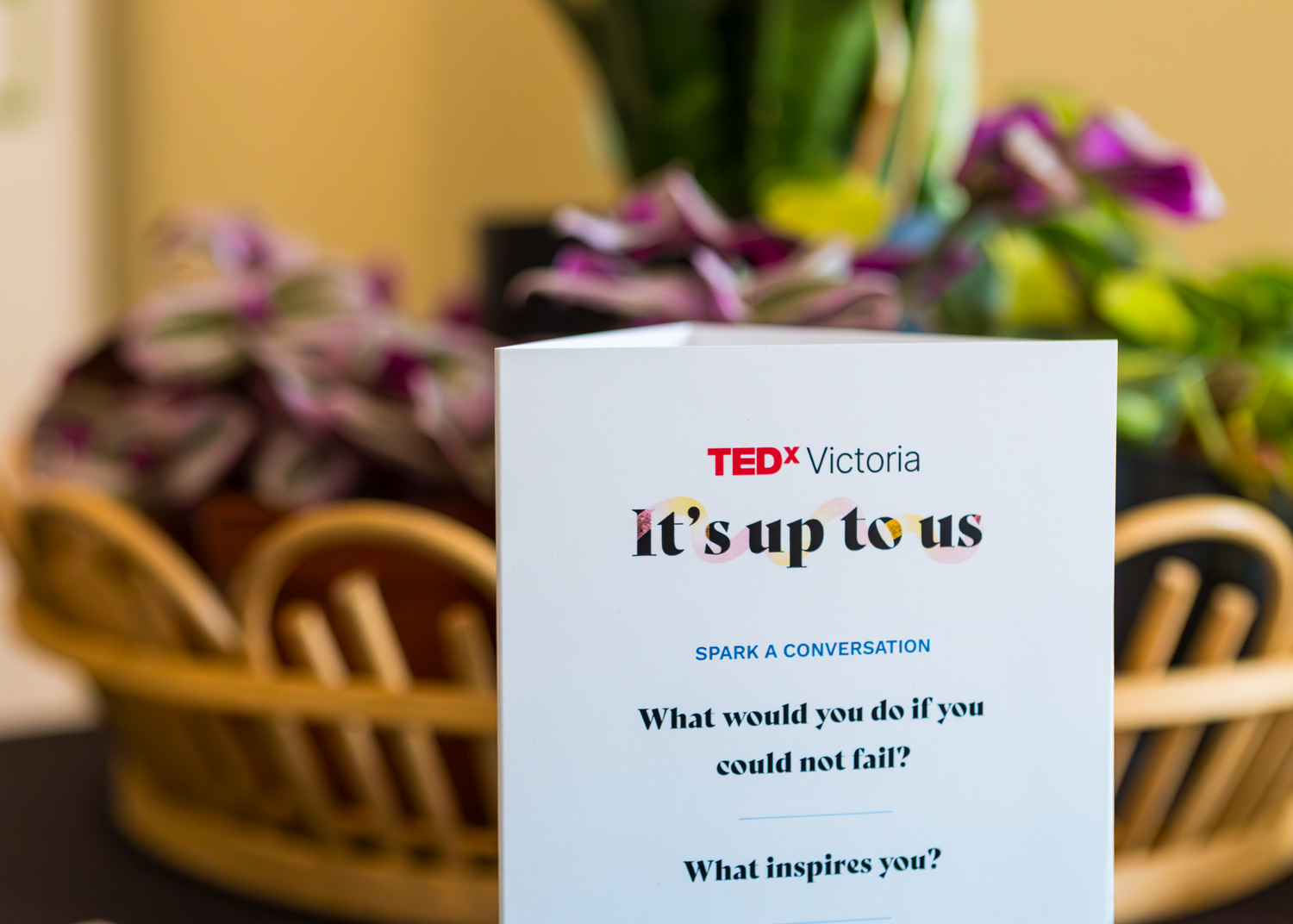 TEDx Victoria program card with 'it's up to us' tagline displayed with flowers in background.