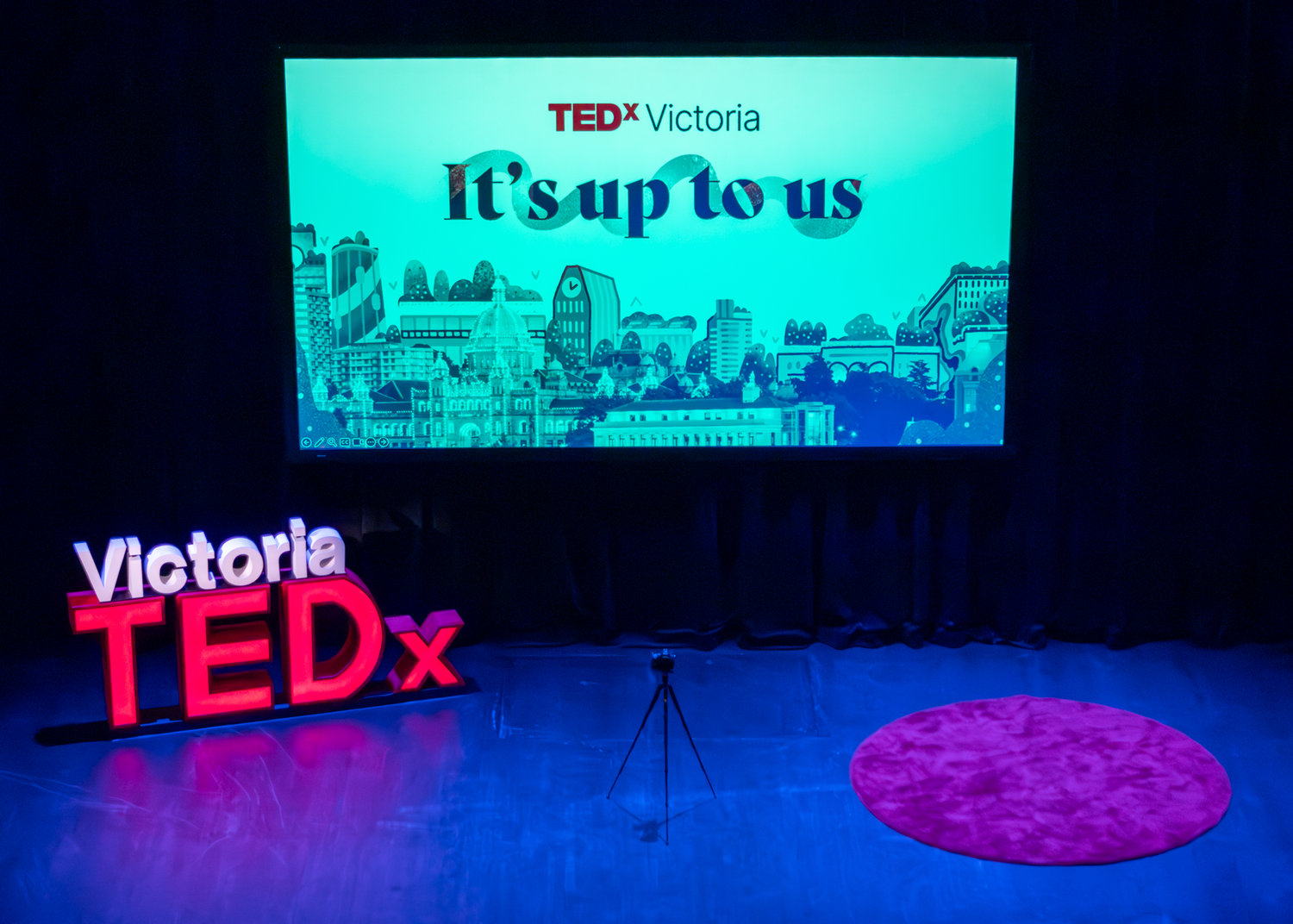 TEDx Victoria stage setup with blue lighting and a red logo display against a dark background.