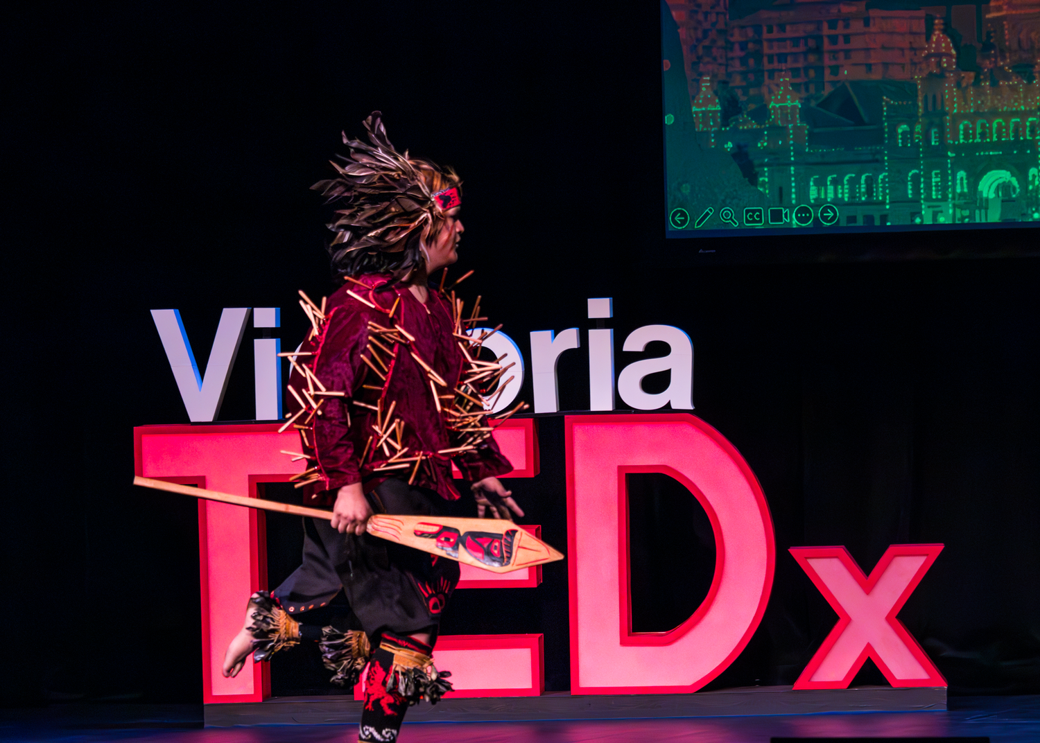Artistic TEDx Victoria logo display with red illumination against a dark cityscape background.