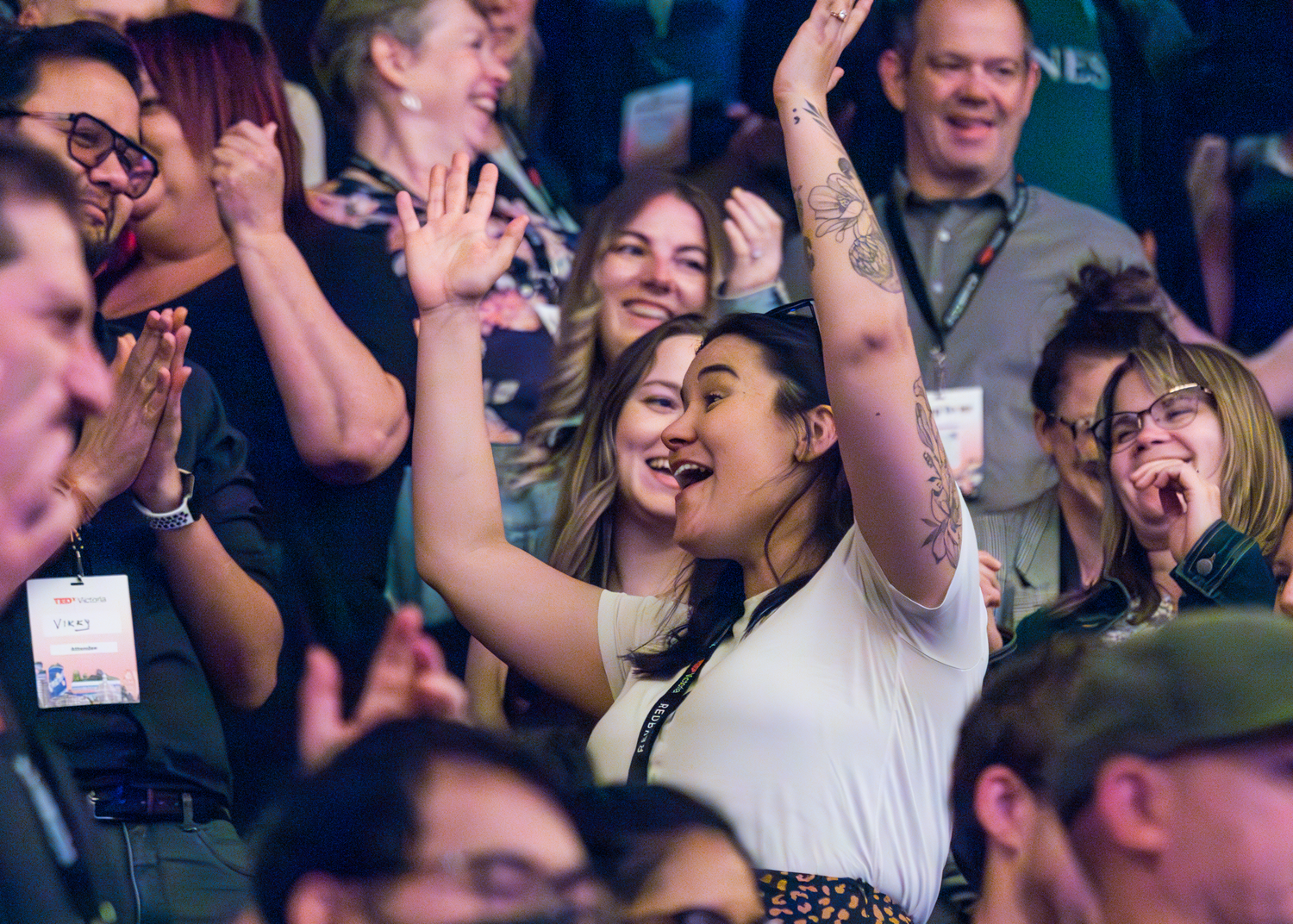 Enthusiastic audience members cheer and raise hands during a TEDx event.