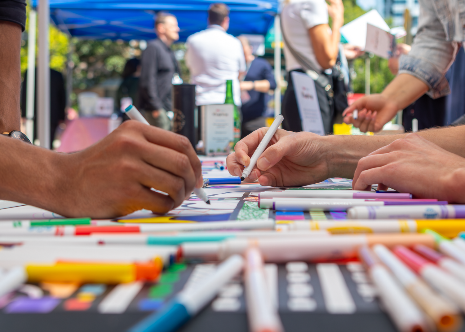 Close-up of hands signing documents with colorful pens and markers spread on a table.