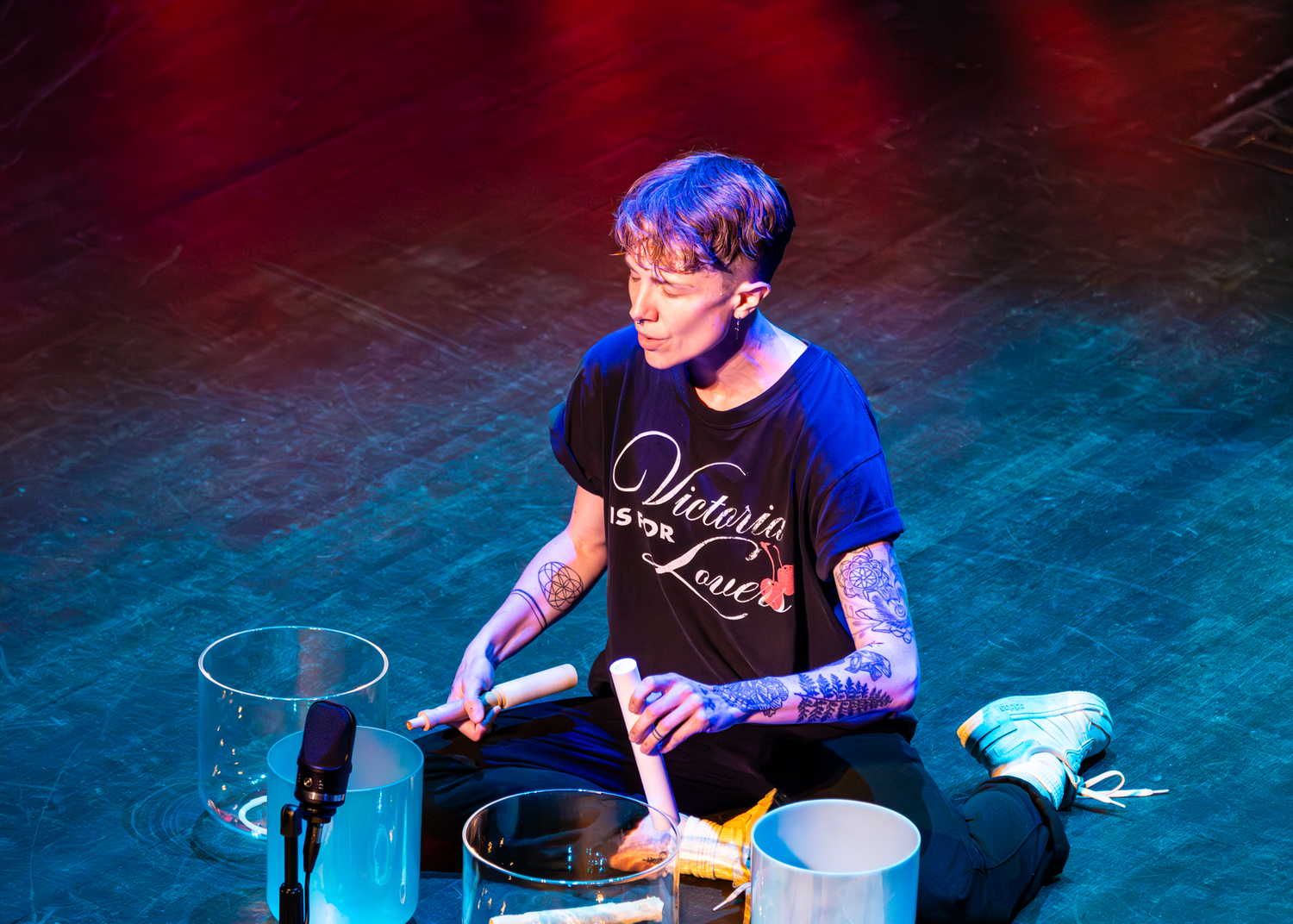A drummer performs on stage with dramatic red and blue lighting effects.