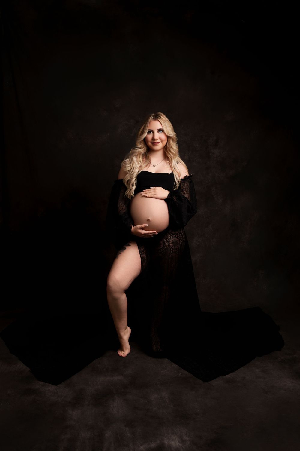 Artistic maternity silhouette in black lace against moody dark background.