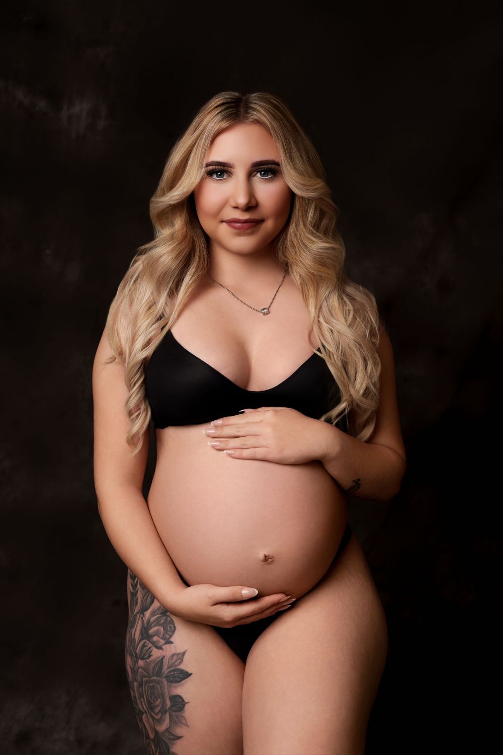 Intimate maternity boudoir portrait in black lingerie against dark background.