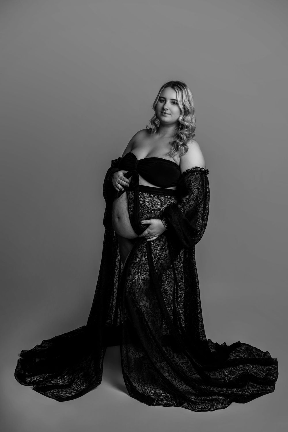 Dramatic black and white maternity portrait with flowing lace robe.