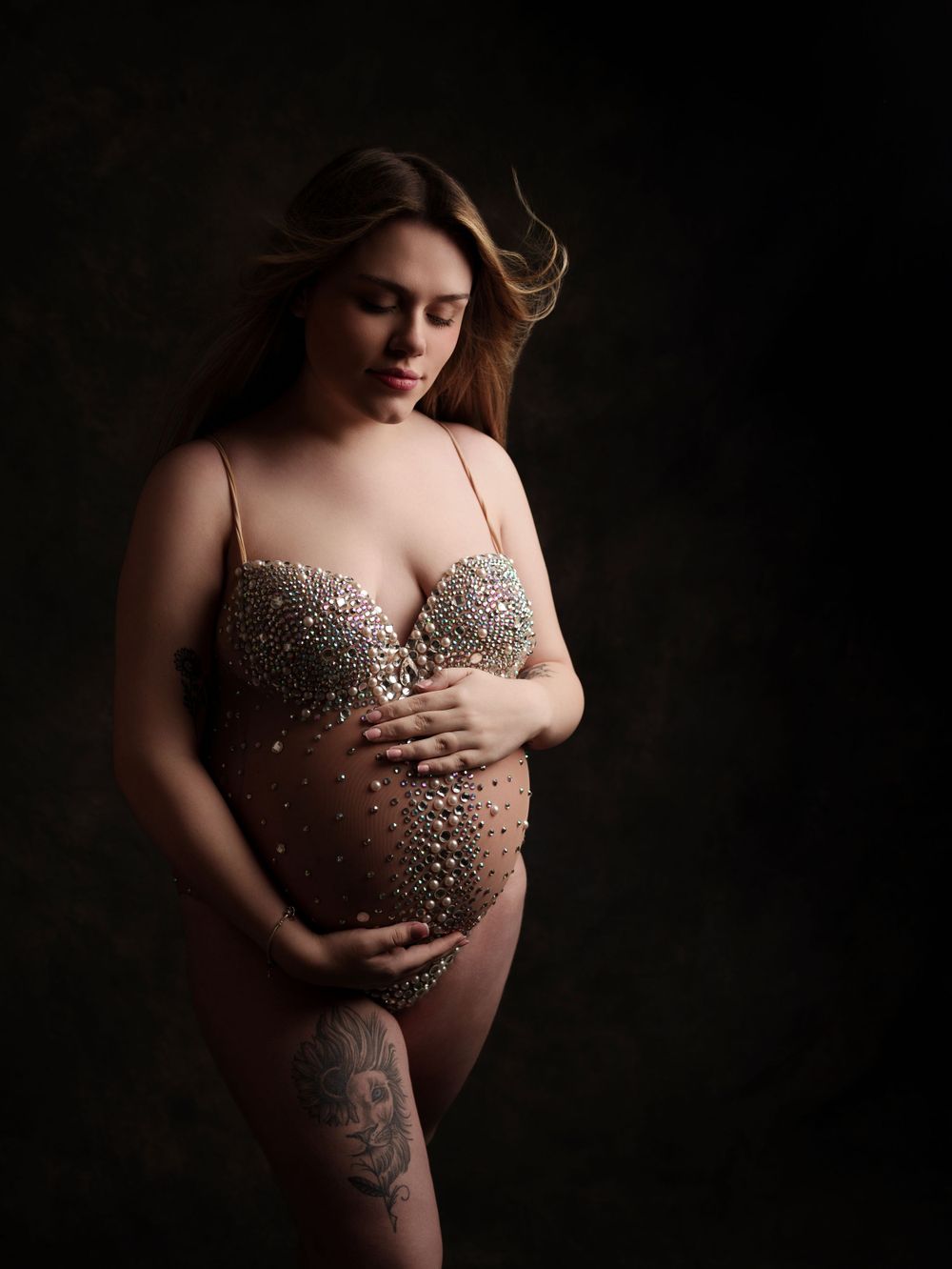 Dramatic maternity photo with glittering bodysuit against dark background.