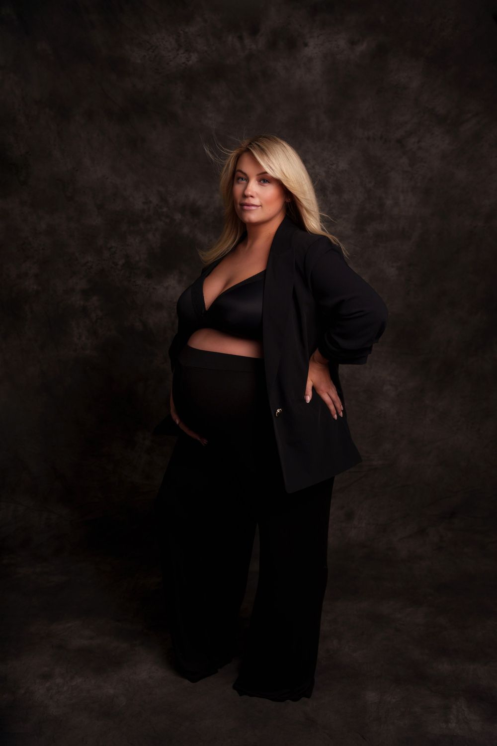 Elegant maternity portrait in black blazer against dark background.