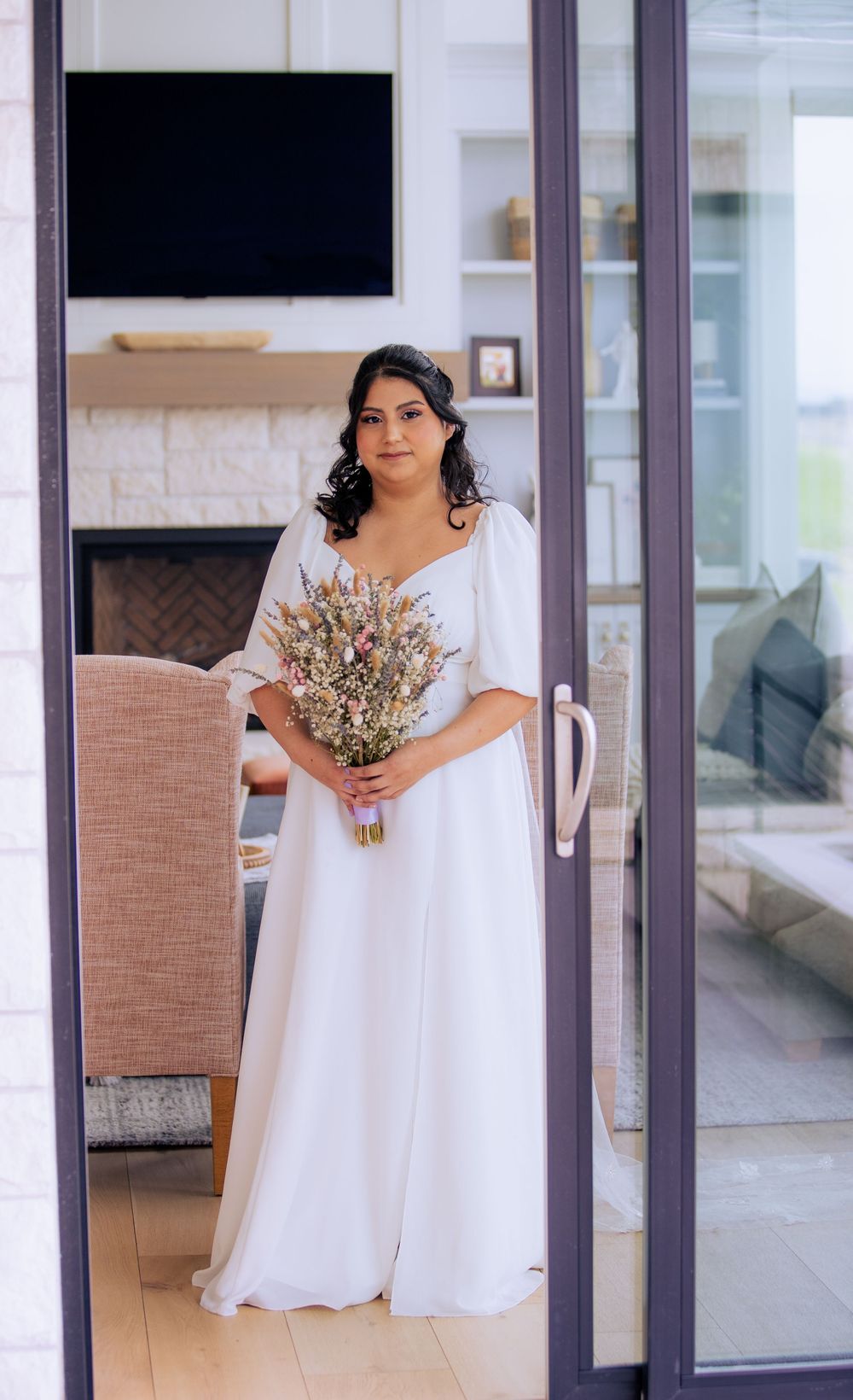 Person in a flowing white dress holding a dried flower bouquet in a modern interior space.